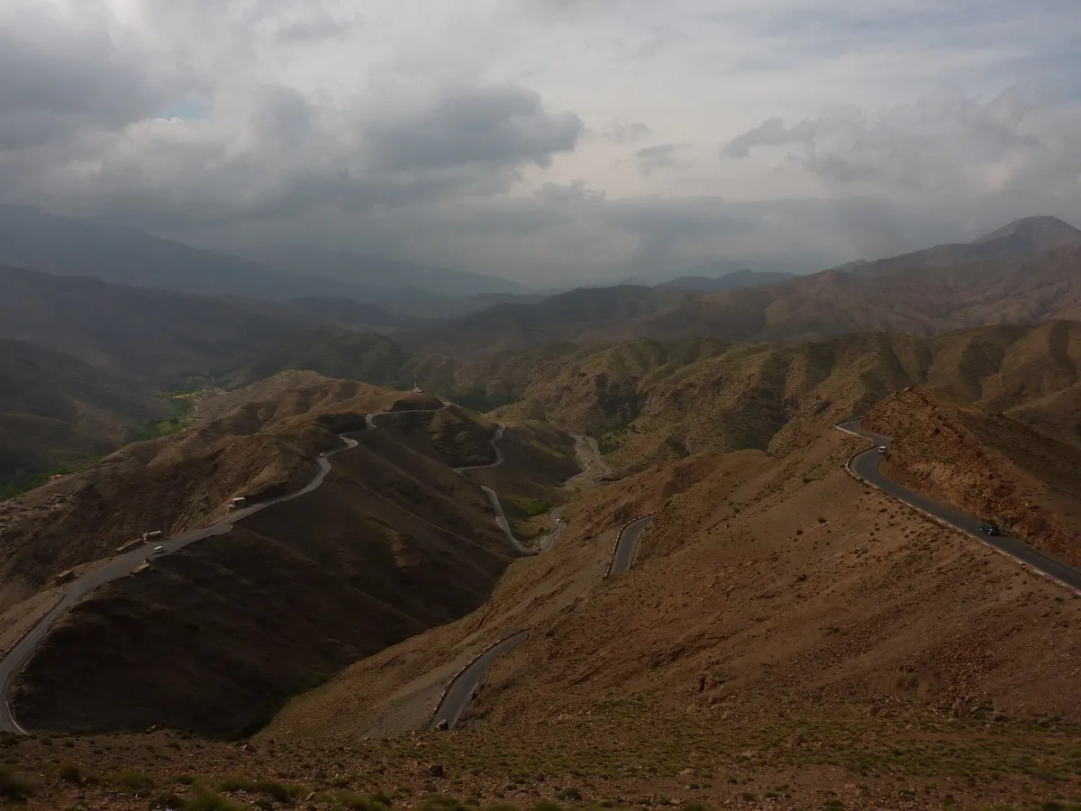 Hairpin bends of the Tizi n'Tichka road cut into a bare mountainside under a storm sky